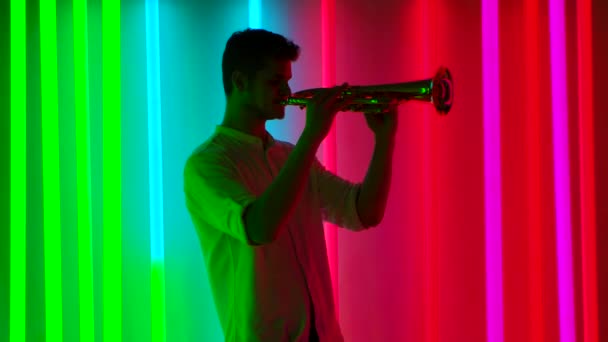 Muestra de música y luces. Un trompetista profesional realiza un concierto de música en un estudio oscuro con tubos de neón multicolores brillantes. Concepto de vida nocturna. Movimiento lento. — Vídeos de Stock
