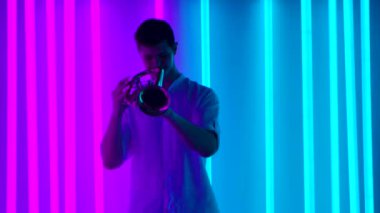 Profesyonel bir trompetçiden caz solo performansı. Beyaz gömlekli bir adam, karanlık bir stüdyoda, parlak neon ışıkların arka planına karşı gösteri yapıyor. Müzikal şov. Yavaş çekim.