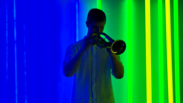 Concerto solista jazz di un trombettista professionista. Un uomo in camicia bianca si esibisce in uno studio buio sullo sfondo di luci al neon luminose. Uno spettacolo musicale. Rallentatore. — Video Stock