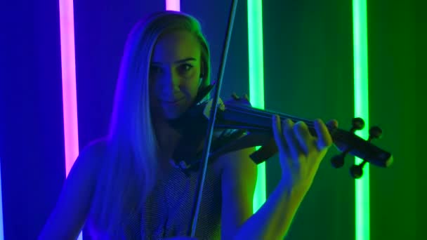 Professionelle Live-Performance einer Geigerin mit einem Konzert klassischer Musik. Junge Frau posiert in einem dunklen Studio vor dem Hintergrund heller Neonlichter. Aus nächster Nähe. Zeitlupe. — Stockvideo
