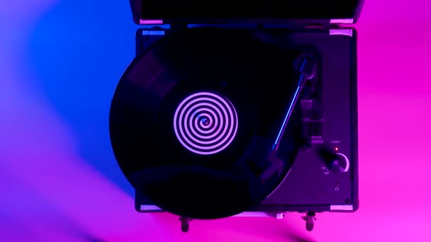 黑胶唱片旋转和播放音乐在dj转盘与彩色标签的中心板。在明亮的霓虹灯的光芒中俯瞰乙烯盘.靠近点慢动作. — 图库视频影像