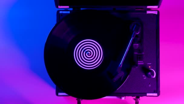 Top view zwart vinyl plaat spinnen en muziek af te spelen op de dj draaitafel. Retro draaitafel tegen een achtergrond van felgekleurde neon lichten. Sluit maar af. Langzame beweging. — Stockvideo