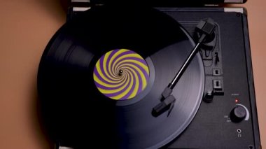 Kahverengi arka planda plakla müzik çalan eski güzel görünümlü turntable. Etiketteki sarı mor hipnotik çemberli siyah plak yavaş çekimde dönüyor. Kapat..