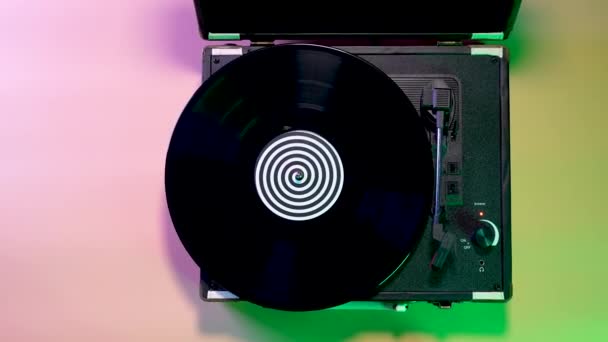 Top view of a music player with a spinning vinyl record against a backdrop of bright neon lights. The moment of approaching a rotating vinyl plate close up. Slow motion. — Stock Video