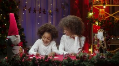 Afrikalı Amerikalı anne ve küçük kızı Noel Baba 'ya mektup yazıp gülümsüyor. Mutlu aile fotoğrafları, yeni yıl kutlaması konsepti..