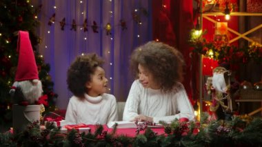 Afrikalı Amerikalı anne ve küçük kızı bir kitap okuyup mutlu bir şekilde sarılıyorlar. Mutlu aile fotoğrafları, yeni yıl kutlaması konsepti..