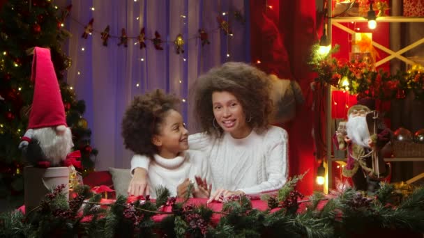 Afroamerikanische Mutter und ihre kleine Tochter reden miteinander und starren freudig in die Kamera. Glückliches Familienporträt, Konzept für die Neujahrsfeier. — Stockvideo