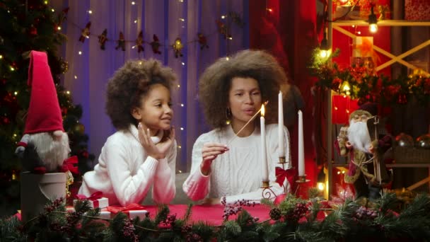 Fröhliche afroamerikanische Mutter und kleine Tochter entzünden weiße Kerzen mit Wow-Entzücken-Emotionen. Glückliches Familienporträt, Konzept für die Neujahrsfeier. — Stockvideo