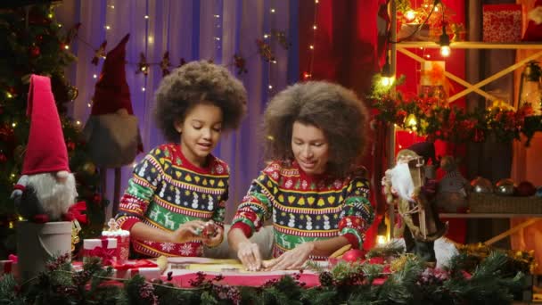 Afro-Amerikaanse moeder en dochter in heldere vakantie truien snijden feestelijke zelfgemaakte koekjes uit deeg. Gelukkig familieportret, Nieuwjaarsviering concept. — Stockvideo