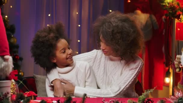 Maman afro-américaine et sa petite fille en pull blanc se serrent dans leurs bras et se regardent. Heureux portrait de famille, concept de célébration du Nouvel An. Gros plan. — Video