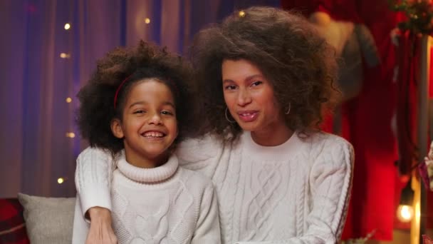 Maman afro-américaine et petite fille en pull blanc se parlent et regardent la caméra avec plaisir. Heureux portrait de famille, concept de célébration du Nouvel An. Gros plan. — Video