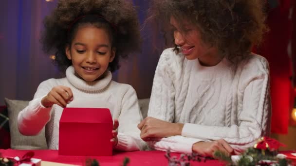 Afroamerikansk mamma och dotter i vita tröjor med glädje packa brevet om jultomten i ett kuvert. Glad familjeporträtt, nyårsfirande koncept. Närbild. — Stockvideo