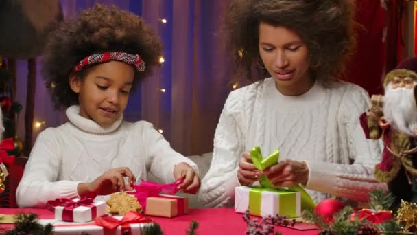 Beyaz kazaklı Afrikalı anne ve küçük kız hediye kutuları süsler ve bayram papyonları bağlarlar. Mutlu aile fotoğrafları, yeni yıl kutlaması konsepti. Kapat.. — Stok video