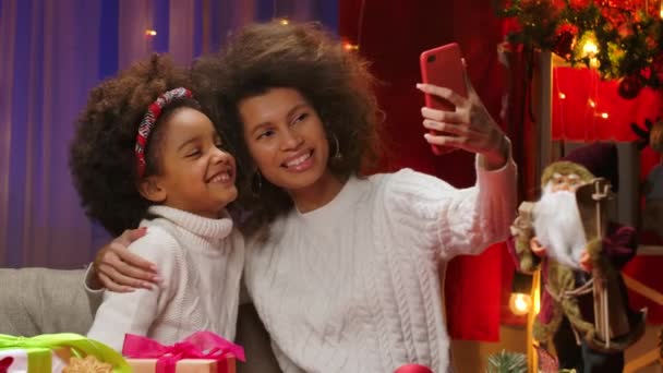 Mãe afro-americana e filha pequena em camisolas brancas se divertindo posando e tirando selfie no smartphone. Retrato de família feliz, conceito de celebração de Ano Novo. Fechar. — Vídeo de Stock