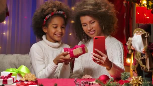Mamma afroamericana e figlioletta in maglioni bianchi che parlano via videochiamata sul loro smartphone. Felice ritratto di famiglia, concetto di celebrazione di Capodanno. Da vicino.. — Video Stock