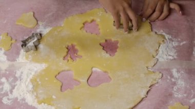 Küçük Afrikalı Amerikalı bir kızın elleri geleneksel Noel kurabiyeleri için hamurdan heykelcikler oyuyor. Una bulanmış mutfak masası. Yavaş çekim.