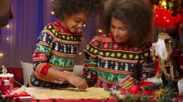 African American mom and little daughter in bright holiday sweaters cut festive homemade cookies from dough. Happy family portrait, New Years celebration concept. Close up. — Stock Video