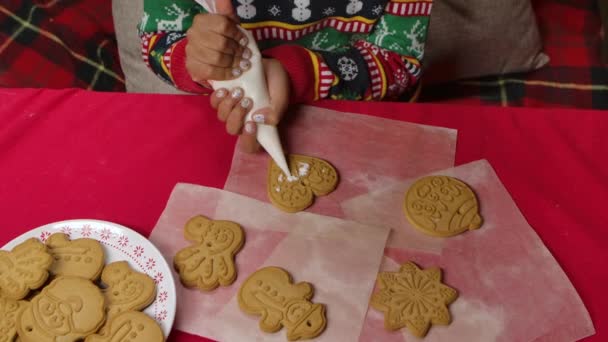 Маленька афроамериканська дівчинка, одягнена у різдвяний светр, гладить традиційне різдвяне печиво. Дитина на задньому плані кухні прикрашена різдвяними святами. Закрийся. Повільний рух. — стокове відео