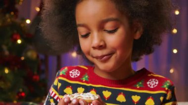 Tatlı Afrikalı Amerikalı kız geleneksel jöleli Noel kurabiyelerinin tadını çıkarıyor. Mutlu yeni yıl tatili ve sıcak aile akşamları kavramı. Kapatın. Yavaş çekim.