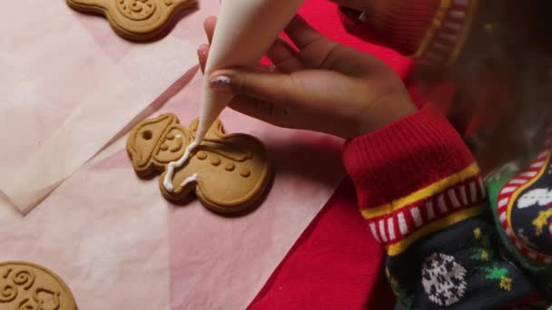 Vista superior de una niña afroamericana en un suéter estampado de Año Nuevo decora una galleta de Navidad tradicional con hielo. De cerca. Movimiento lento. — Vídeos de Stock