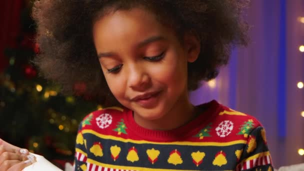 Cute curly haired African American girl enjoys trying the icing to decorate the cookies. Concept of merry new year holidays and warm family evenings. Close up. Slow motion. — Stock Video