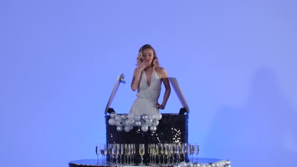 マーリン・モンローの姿をしたチャーミングな若い女性がブラックケーキから現れる。薄い青の背景にスタジオでブロンドポーズ。お祝い、企業パーティー、誕生日。閉めろ。スローモーション — ストック動画