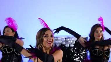 Muhteşem seksi kadınlar büyük siyah bir pastanın yanında neşe içinde dans ediyorlar. Erotik kostümlü burlesque dansçıları mavi bir stüdyoda poz veriyorlar. Şenlikli tiyatro dans gösterisi. Kapatın. Yavaş çekim.