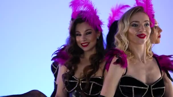 Wunderschöne sexy Burlesque-Tänzerinnen posieren verspielt neben einer großen schwarzen Torte. Heiße Weibchen tanzen auf blauem Studiohintergrund. Festliche theatralische Tanzshow. Aus nächster Nähe. Zeitlupe. — Stockvideo
