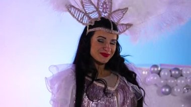 Beyaz Kar Kraliçesi kostümlü ve tüylü başlıklı üç sevimli kadın büyük bir pastanın yanında dans ediyorlar. Dansçılar açık mavi bir stüdyo arka planında poz veriyorlar. Kapatın. Yavaş çekim.