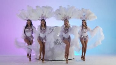 Beyaz Kar Kraliçesi kostümlü ve tüylü başlıklı sevimli kadınlar büyük bir pastanın yanında dans ediyorlar. Dansçılar açık mavi bir stüdyo arka planında poz veriyorlar. Yeni yıl selamları. Yavaş çekim.