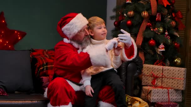 Papai Noel com uma criança sentada em seu colo se comunicar via chamada de vídeo em um smartphone. Fecha. Movimento lento. — Vídeo de Stock