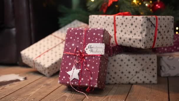 Hermosas cajas de regalo de Navidad en una pila de regalos se encuentran en el suelo de madera debajo del árbol. Los regalos de Año Nuevo, de fiesta y de compras navideñas. Tarjeta de felicitación navideña. De cerca. Movimiento lento. — Vídeo de stock