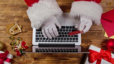 Noel Baba 'nın elleri beyaz eldivenlerle klavyeye ahşap yeni yıl süsleme masasıyla yazı yazıyor. Noel Baba internetten kredi kartıyla alışveriş yaparken dizüstü bilgisayarla çalışır. Kapatın. Yavaş çekim.