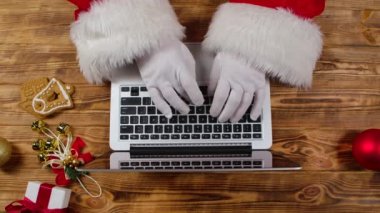 Noel Baba 'nın elleri beyaz eldivenlerle klavyeye ahşap yeni yıl süsleme masasıyla yazı yazıyor. Noel Baba dizüstü bilgisayarla çalışır, mektuplara bakar ve çocuklara hediyeler hazırlar. Kapatın. Yavaş çekim