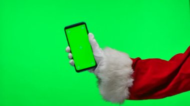 Noel Baba beyaz eldivenler içinde yeşil ekran krom anahtarı olan bir akıllı telefonu dikey pozisyonda tutar. Stüdyoda yeşil bir arka planda izole edilmiş. Ekranı düzelt. Kapatın. Yavaş çekim.