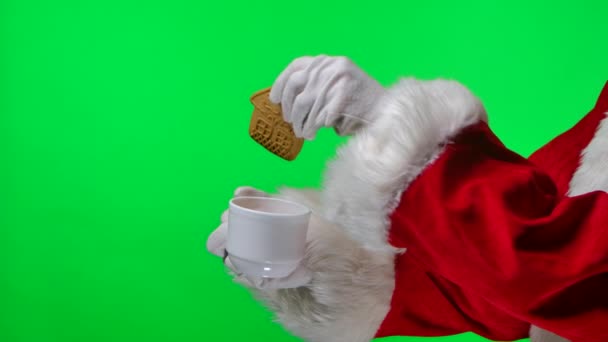 Vista lateral Santa Claus en guantes blancos y traje rojo sostiene la taza de té en sus manos y empapa galletas caseras de Navidad en él. Aislado en una pantalla verde en un estudio. Clave de croma. De cerca. Movimiento lento. — Vídeo de stock
