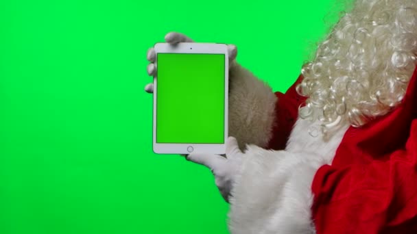 Boční pohled Santa Claus s plnovousem v bílých rukavicích drží tablet ve svislé poloze se zeleným displejem chroma klíčem. Izolované na zeleném pozadí ve studiu. Zesměšňujte displej. Zavřít. Zpomalený pohyb. — Stock video