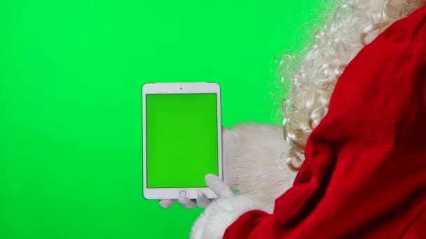 Zijaanzicht Santa Claus met baard in witte handschoenen houdt tablet in verticale positie en wijst vinger met groen scherm chroma sleutel. Geïsoleerd op groene achtergrond in de studio. Sluit maar af. Langzame beweging. — Stockvideo