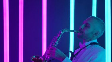 Beyaz takım elbiseli bir adam parlak altın bir saksafon çalar. Karanlık stüdyo parlak pembe ve mavi neon tüplerle aydınlatılır. Neon ışık efektleri. Yan görüş. Ağır çekim, yakın çekim..
