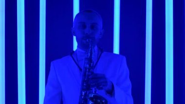 Yetenekli bir saksafoncu altın bir saksafonda caz çalar. Stüdyoda beyaz takım elbiseli bir adam çok renkli neon boruların arka planına karşı. Ağır çekim, yakın çekim..