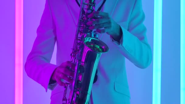 Gyllene skinande saxofon på nära håll. Detaljerade bilder av manliga händer vidrör nycklarna till ett blåsinstrument mot en mörk studio bakgrund med ljusa neonljus. Långsamma rörelser. — Stockvideo