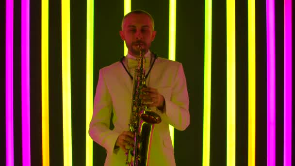 The musician plays the saxophone. Cultural performance of live classical melody by a talented performer. Musician in the studio against the background of multicolored neon pipes. Slow motion, close up — Stock Video