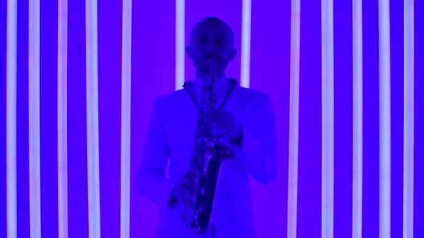 一个身穿白色西服的音乐家在萨克斯风上弹奏爵士乐的画像。在演播室里的萨克斯演奏家，背景是五彩缤纷的霓虹灯管。慢动作，关门. — 图库视频影像