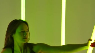 Bir dansçı, parlak renkli neon tüplerle çevrili bir stüdyoda modern bir dans sergiliyor. Elleri ağır çekimde neon tüplere tutunarak dans eden bir kız. Portreyi kapat.