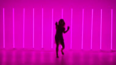 Şeffaf elbiseli bir kızın silueti parlak neon boruların arkasında dans ediyor. Bir dansçı ya da balerin, ağır çekimde modernlik ve bale öğeleriyle dans ediyor..