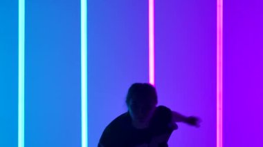 Stüdyoda dans eden genç bir kadın mavi mor arka planda neon ışıklı tüp ile dans ediyor. Modern hareketleri yavaş çekimde yapan bir hip hop dansçısı. Koyu renk siluet. Kapat..