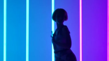 Çok renkli neon tüplerin arkasında dans eden genç ve şık bir kızın silueti. Dansçı modern hareketleri yavaş çekimde gerçekleştirir. Kapat..
