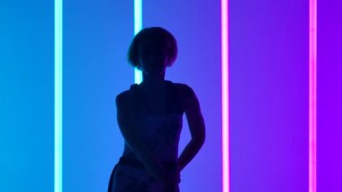 Çok renkli neon tüplerin arkasında dans eden genç ve şık bir kızın silueti. Kız yavaşça kollarını ve omuzlarını hareket ettiriyor. Modern müzik konsepti. Kapat..