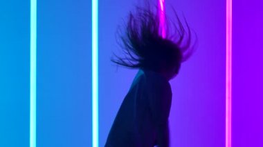 Stüdyoda dans eden uzun saçlı bir kız. Yavaş çekimde renkli neon ışıklarla aydınlatılıyor. Dansçı çağdaş müzikten hoşlanır. Gençlik kültürü ve aktif yaşam tarzı konsepti. Kapat..