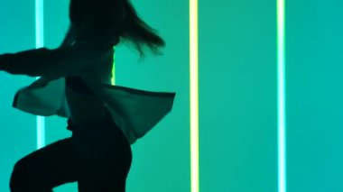 Modern çağın dans öğelerini seslendiren bir dansçının silüeti. Çok renkli neon tüplerin arka planında yavaş çekimde çağdaş dans eden kız. Kapat..